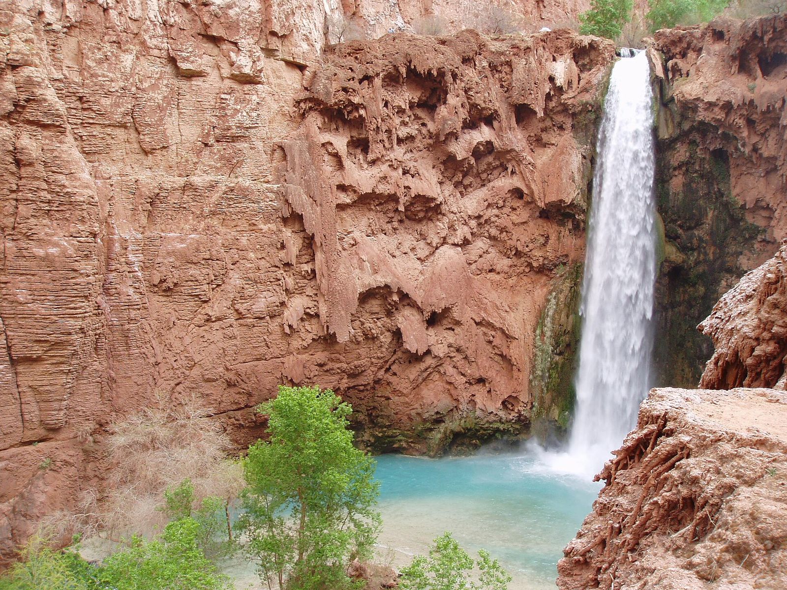 Mooney Falls cascades down towering red sandstone cliffs into a brilliant turquoise pool in Havasupai, Arizona.