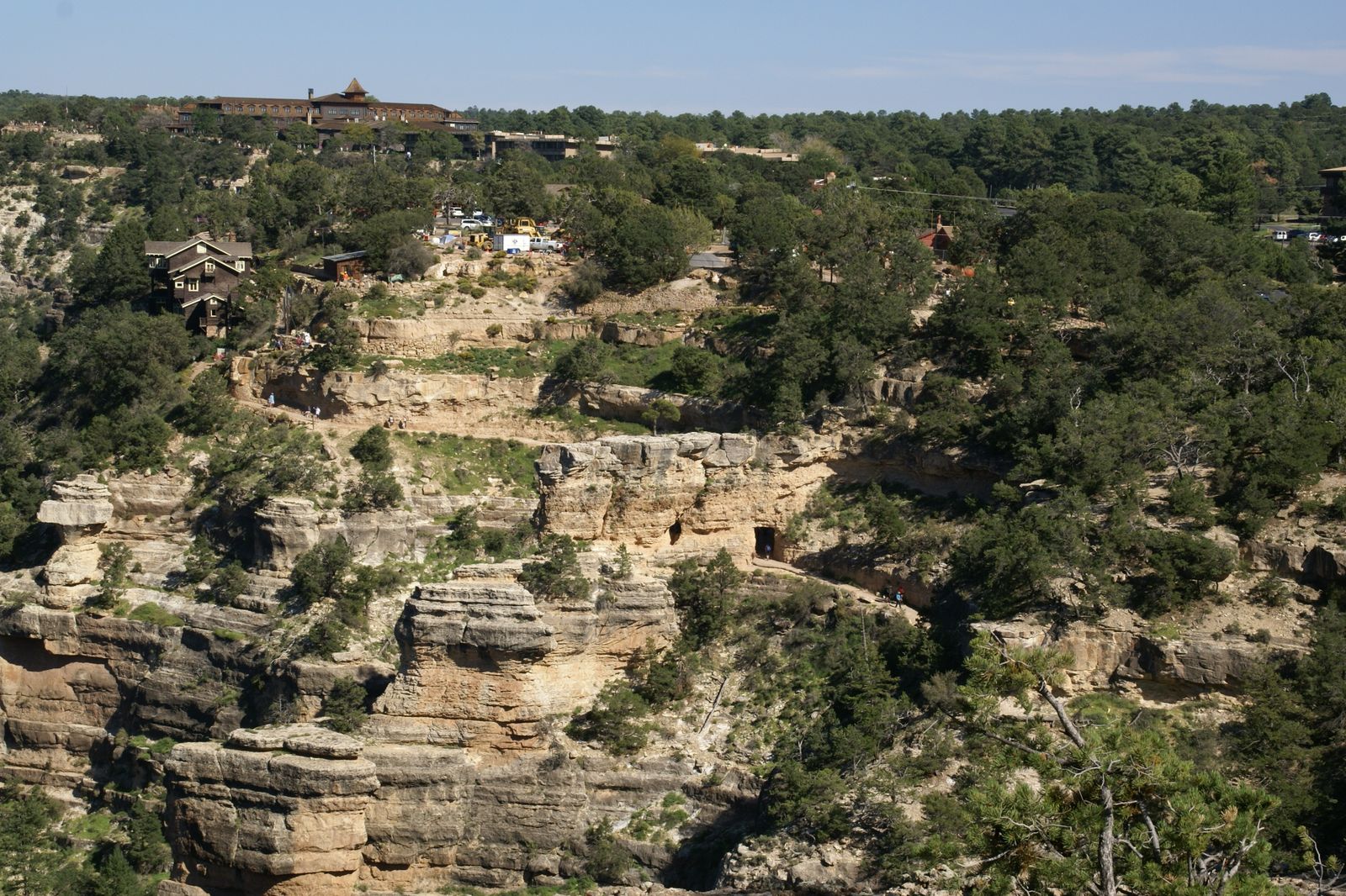 The Bright Angel Trail switchbacks past a rock tunnel below the South Rim, with El Tovar Hotel and Kolb Studio visible on the canyon rim above.