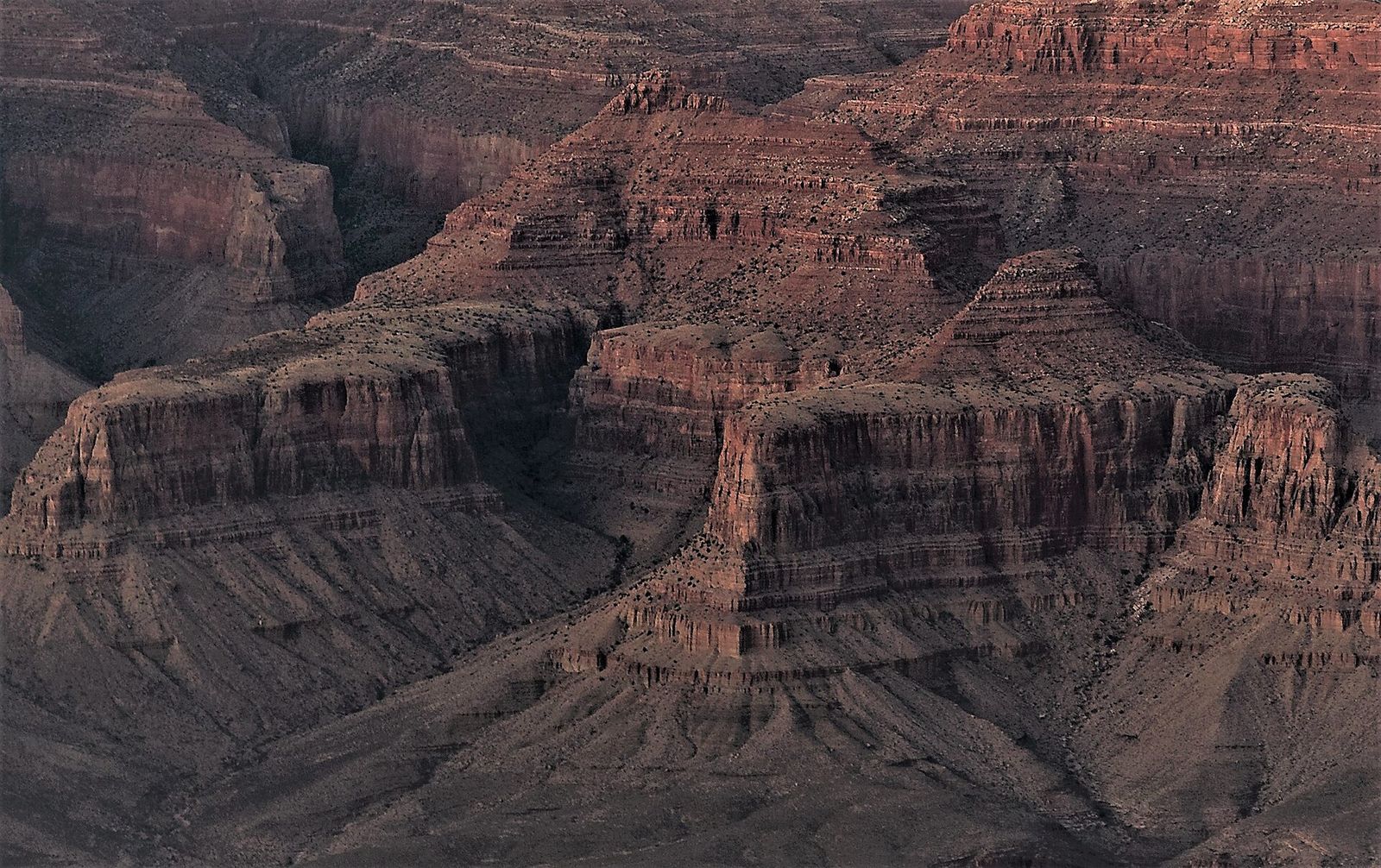 Deeply layered red rock buttes and canyon walls stretch across the Grand Canyon in dramatic shadow and light.