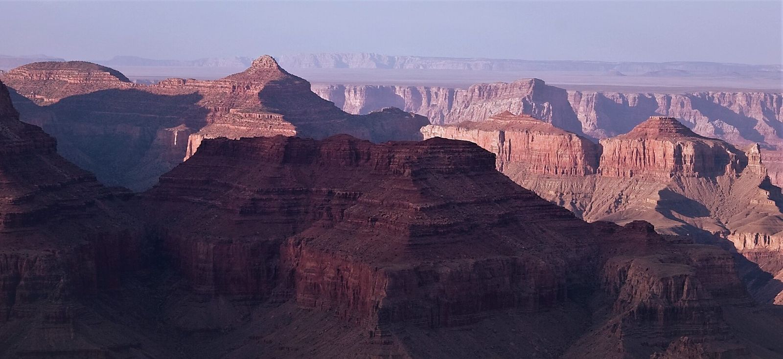 Grand Canyon Buttes and Canyon Layers at Dusk Sweeping Grand Canyon panorama showing layered red rock buttes and deep shadowed gorges under a hazy sky.