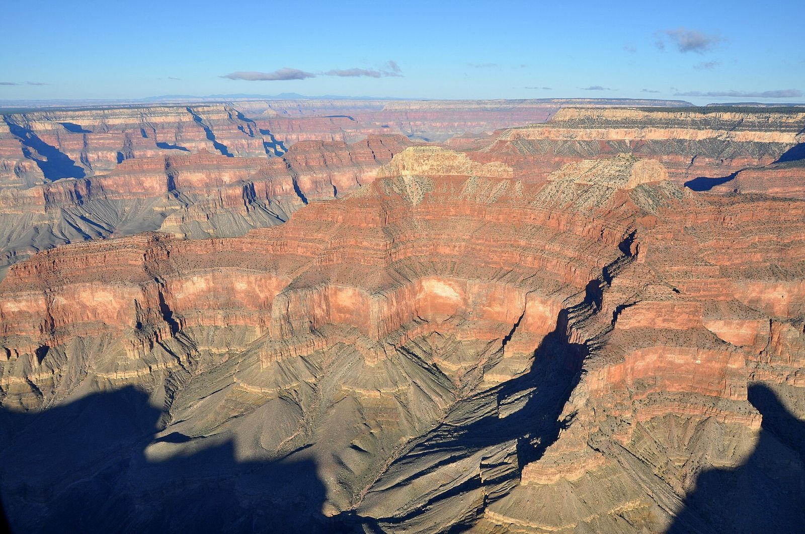 Aerial View of Grand Canyon Layered Canyon Walls A sweeping aerial view of Grand Canyon's layered red rock walls and vast canyon depths under blue sky.
