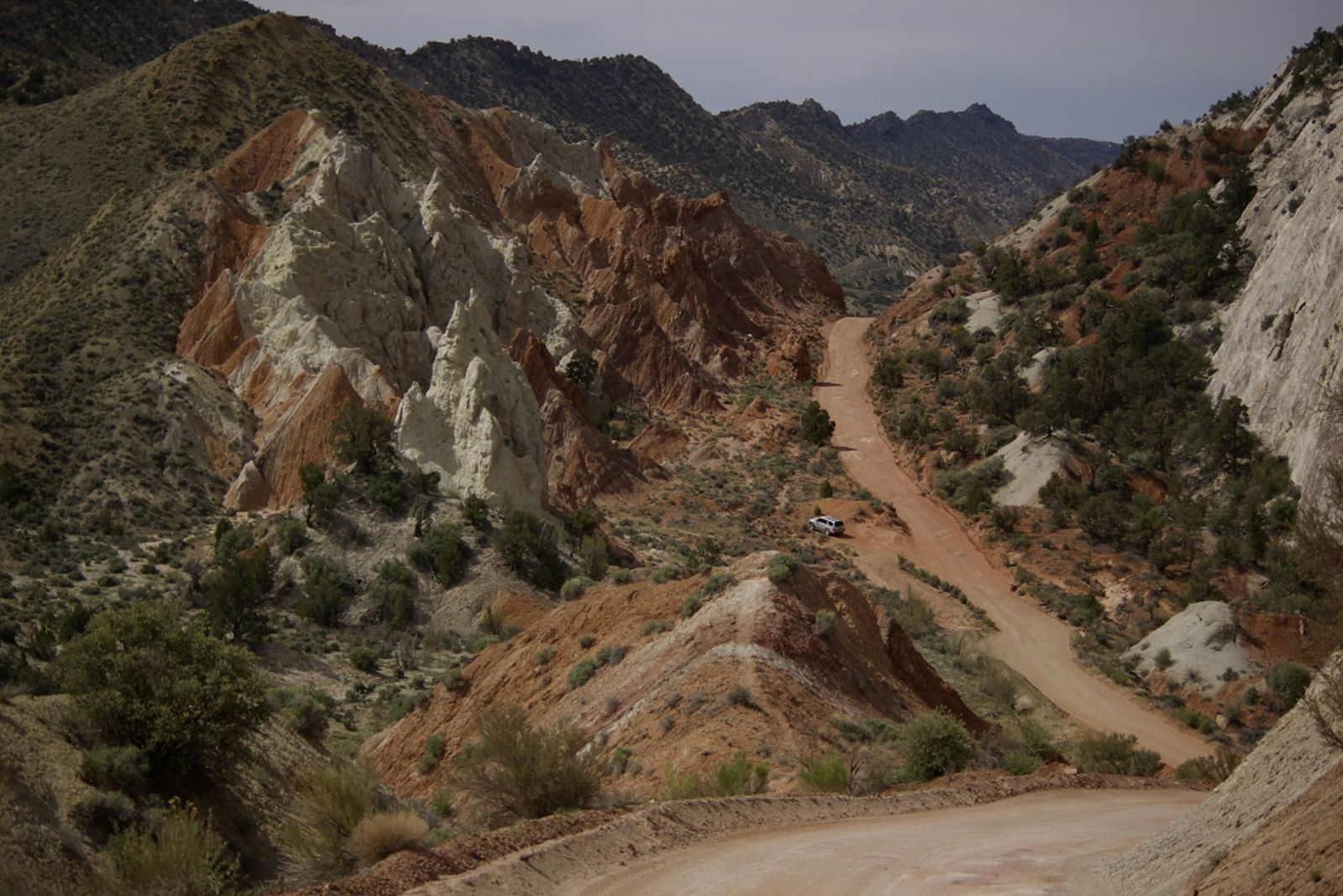 A lone vehicle navigates the winding dirt road through Cottonwood Canyon's dramatic red and white sandstone formations.