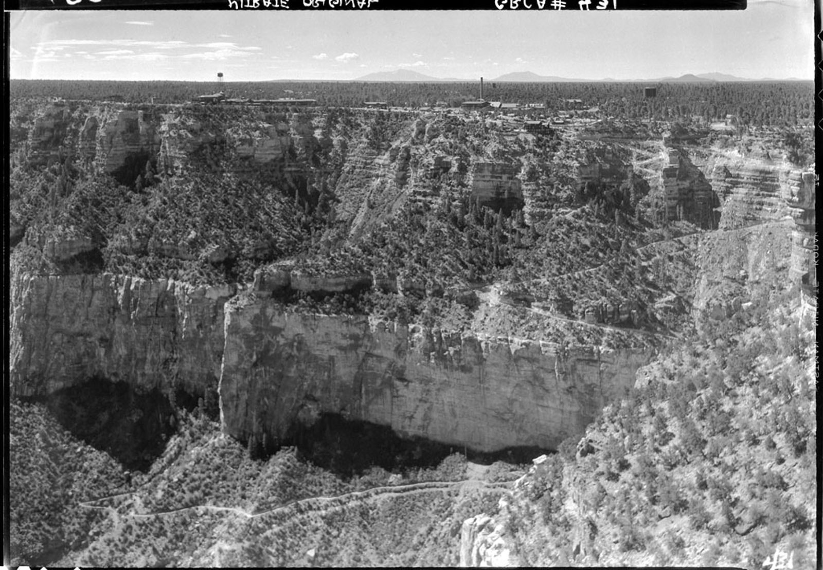 A vintage black-and-white aerial photograph of Bright Angel Trail winding through the Grand Canyon's South Rim canyon walls.
