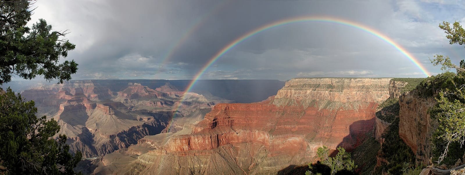 A full double rainbow arches dramatically over the Grand Canyon's layered red rock formations from Pima Point.
