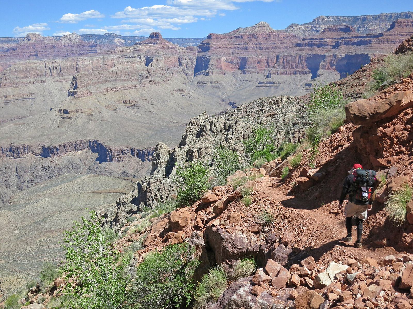 A backpacker with a full pack descends the rocky Hermit Trail into the Grand Canyon's vast layered interior.