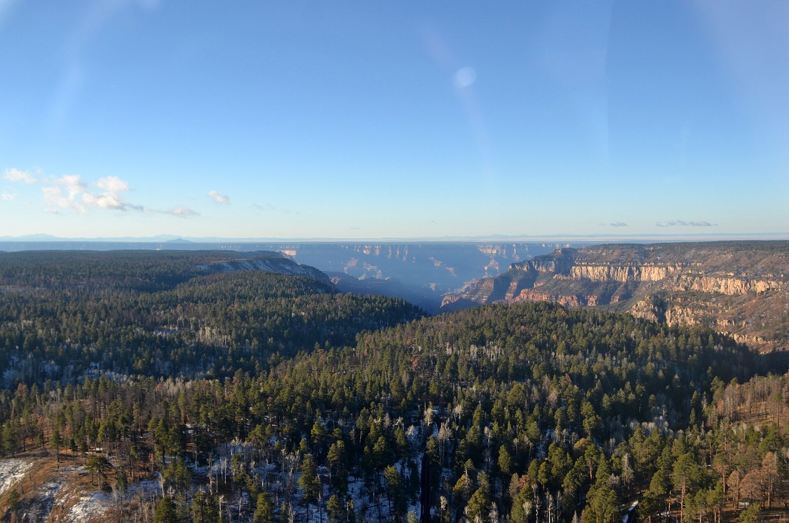 Aerial winter view of the Grand Canyon North Rim with snow-dusted ponderosa pine forest and canyon depths below.