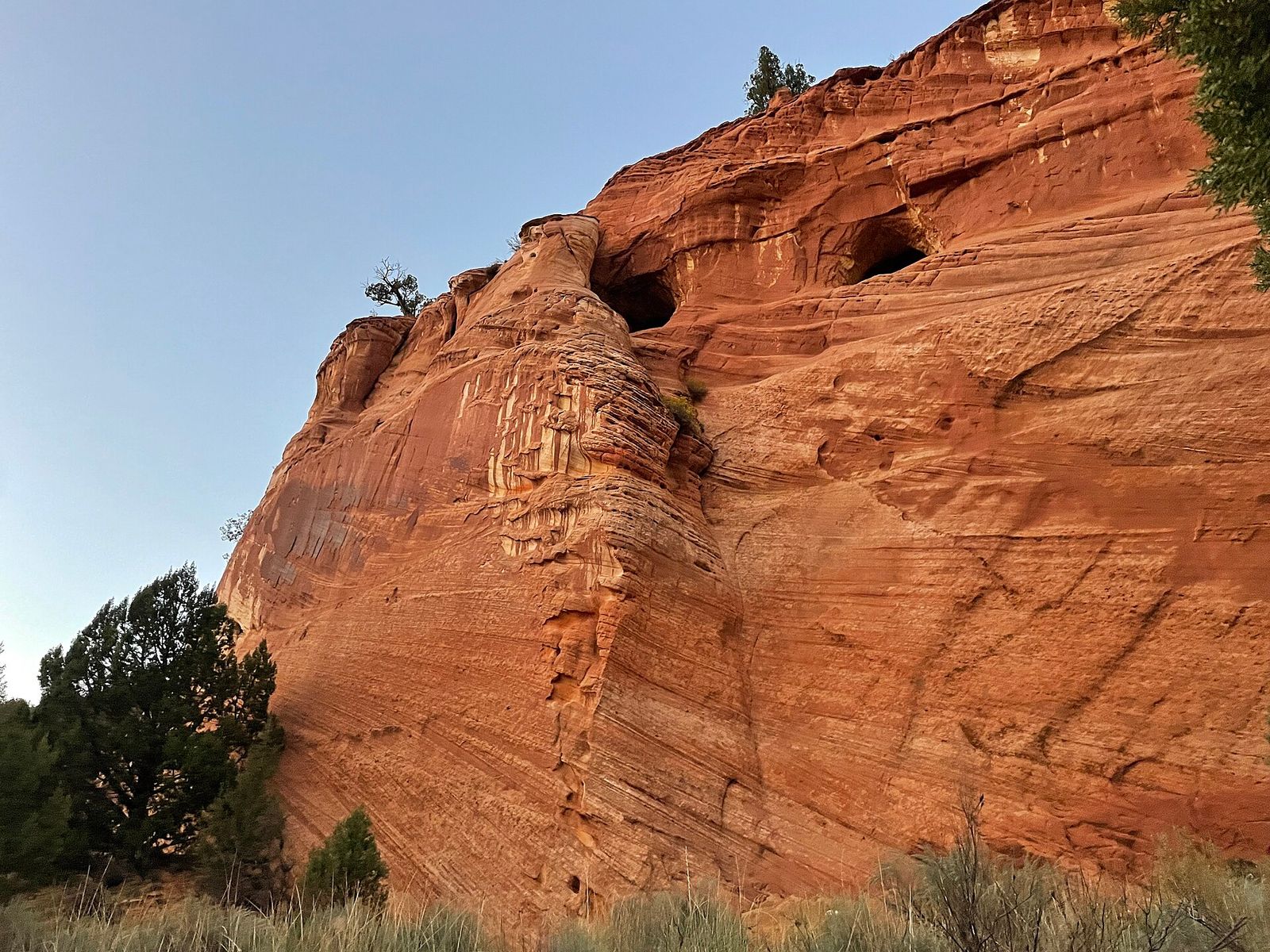 Towering red sandstone cliffs with natural cave openings near Kanab, a popular stop on the way to the Grand Canyon.