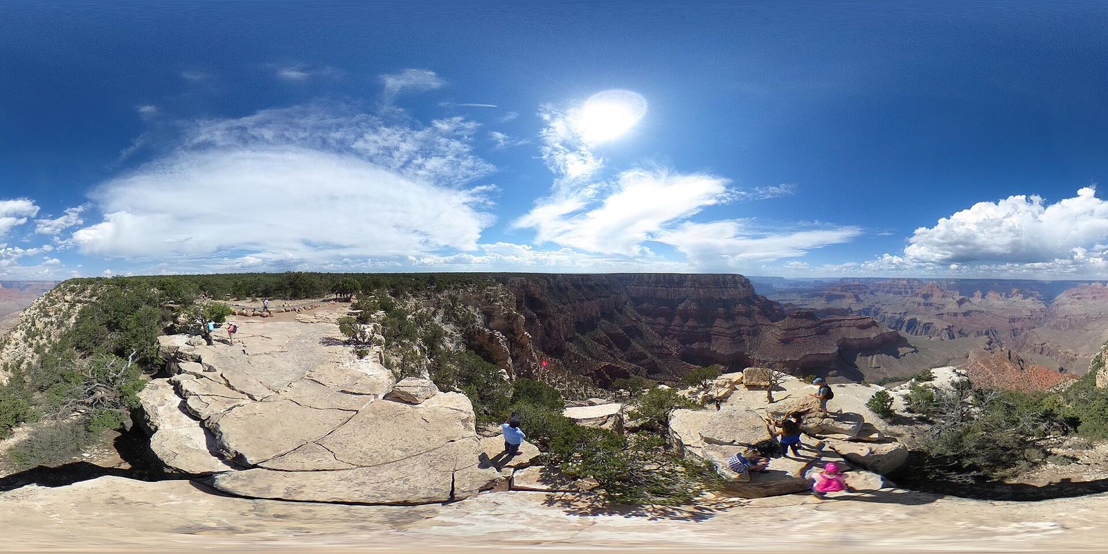 Grandeur Point Overlook, Grand Canyon South Rim Visitors exploring the rocky rim at Grandeur Point overlook on the Grand Canyon South Rim under blue skies.