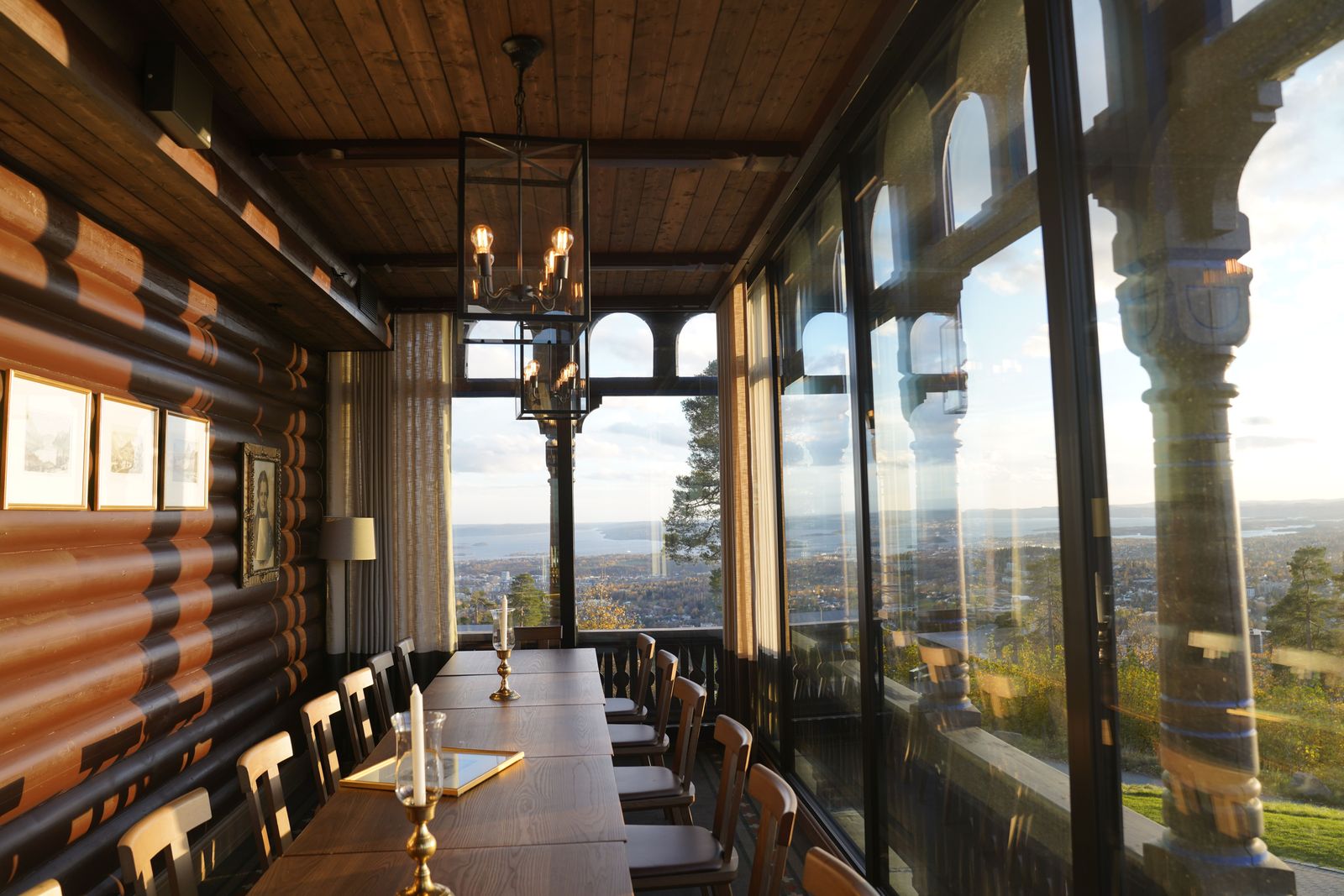 A wood-paneled lodge dining room with a long table and large windows looking out over a scenic view.