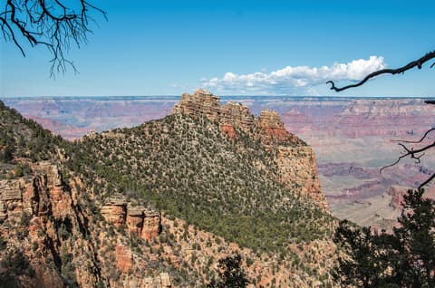 Sinking Ship butte rises above layered red rock canyon walls at Grand Canyon National Park under blue skies.