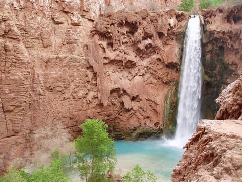 Mooney Falls cascades down towering red sandstone cliffs into a brilliant turquoise pool in Havasupai, Arizona.