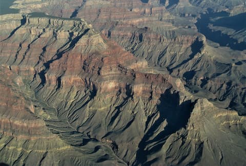 A sweeping aerial view of Grand Canyon's layered red rock buttes and shadowed canyon depths in Arizona.