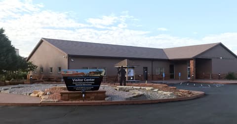 The Grand Staircase-Escalante National Monument Visitor Center entrance sign in Kanab, Utah, under a partly cloudy sky.