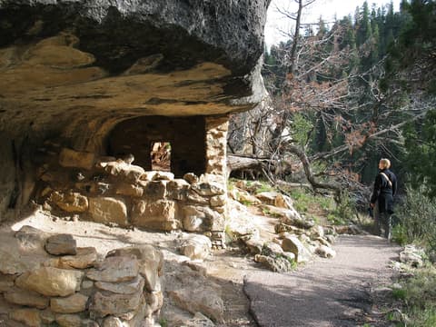A hiker gazes up at ancient cliff dwelling ruins tucked beneath a limestone overhang at Walnut Canyon, Arizona.