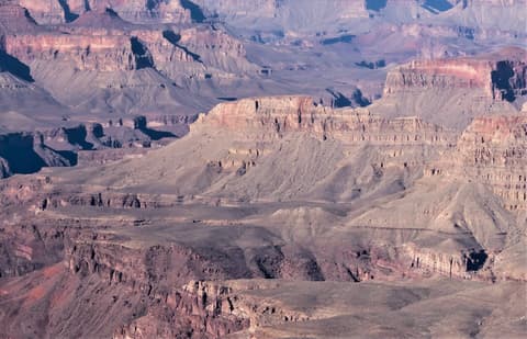 Sweeping aerial view of layered Grand Canyon buttes and rock formations in muted pink and purple tones.