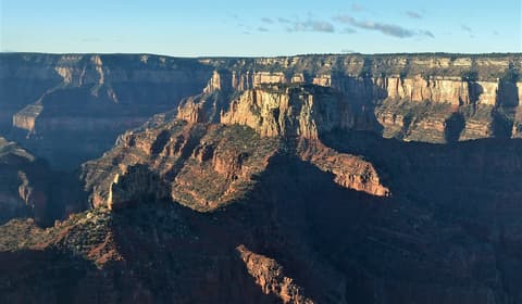 Dramatic Grand Canyon buttes and layered red rock cliffs glow in warm early light from the North Rim overlook.