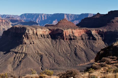 Layered red rock buttes and canyon walls stretch deep into Grand Canyon National Park under a clear blue sky.