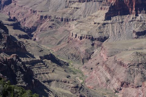 Sweeping view of Grand Canyon's inner canyon revealing dramatic layered rock formations and a winding green valley below.