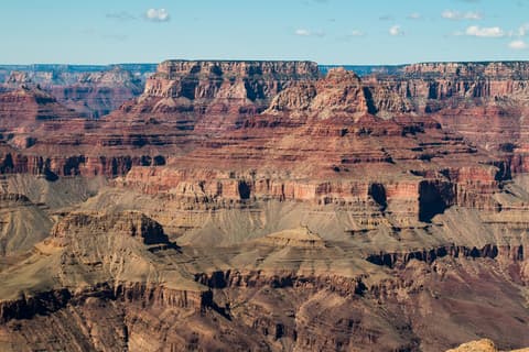 Sweeping Grand Canyon view showing layered red and gray rock formations including Vishnu Temple under a blue sky.