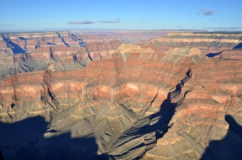 A sweeping aerial view of Grand Canyon's layered red rock walls and vast canyon depths under blue sky.