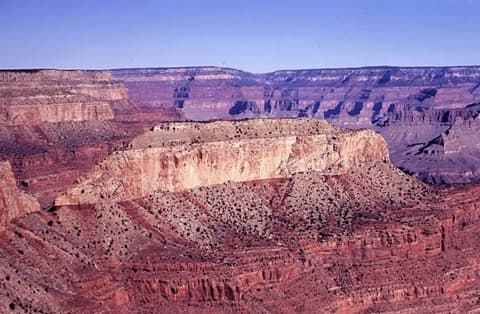 Layered red rock canyon walls and a flat-topped butte stretch deep into Grand Canyon National Park under clear blue skies.