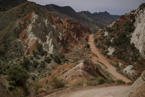 A lone vehicle navigates the winding dirt road through Cottonwood Canyon's dramatic red and white sandstone formations.