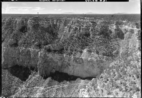 A vintage black-and-white aerial photograph of Bright Angel Trail winding through the Grand Canyon's South Rim canyon walls.