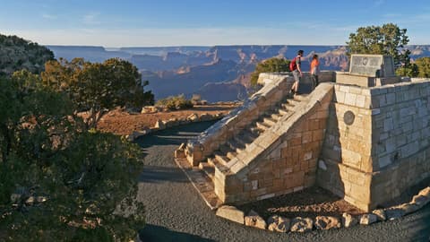 Two visitors stand atop the historic Powell Point Memorial overlook on the Grand Canyon South Rim.