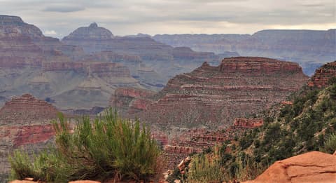 Sweeping Grand Canyon view of Newton Butte's layered red rock formations beneath a dramatic overcast sky.