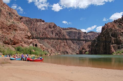 Colorful rafting boats pulled ashore on a sandy Colorado River beach below the Black Bridge at Phantom Ranch.