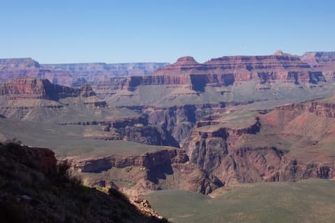 Sweeping Grand Canyon interior view showing layered red rock buttes, the Tonto Platform, and a clear blue sky.