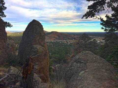 A jagged rock spire frames a sweeping view of Flagstaff, Arizona, surrounded by ponderosa pine forest.