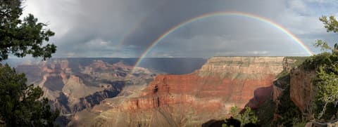 A full double rainbow arches dramatically over the Grand Canyon's layered red rock formations from Pima Point.