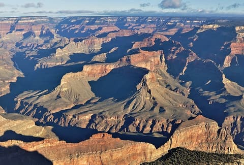 Sweeping panoramic view of Grand Canyon buttes and layered rock formations under a partly cloudy sky.