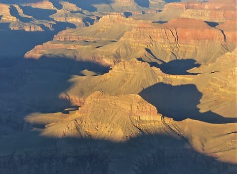 Dramatic golden light and deep shadows sculpt the layered sandstone buttes of Grand Canyon's inner canyon.