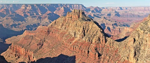 A towering sandstone butte rises above the layered red rock formations of Grand Canyon National Park's South Rim.
