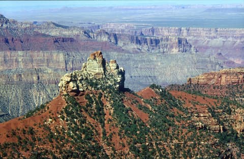 Brady Peak butte rises above red slopes on the Grand Canyon North Rim with layered canyon walls stretching toward the horizon.