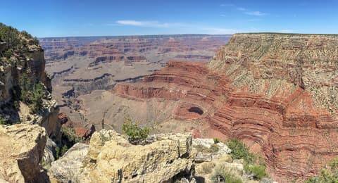 A sweeping panoramic view of Grand Canyon's layered red rock formations under a clear blue sky.