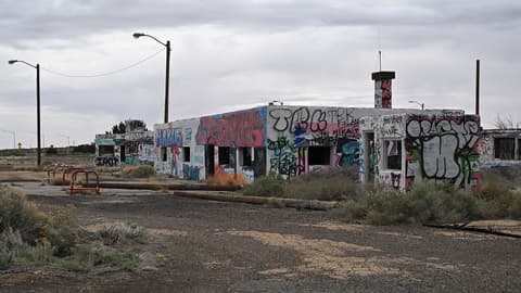 An abandoned graffiti-covered building sits along historic Route 66 near Twin Arrows, Arizona, surrounded by desert scrub.
