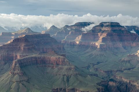 Dramatic layers of red rock buttes and mesas stretch across Grand Canyon National Park beneath billowing storm clouds.