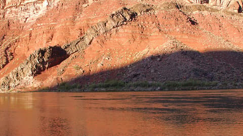 The Colorado River flows past ancient Hakatai Shale canyon walls with dramatic layered red rock formations.