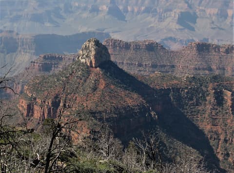 A rocky butte rises above forested canyon ridges with hazy layered walls stretching deep into Grand Canyon National Park.