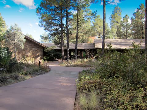 A curved walkway leads through ponderosa pine forest to a rustic stone building at the Arboretum at Flagstaff, Arizona.