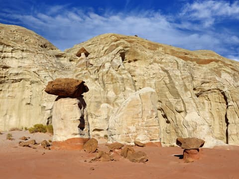 A toadstool hoodoo with a balanced caprock stands before towering white sandstone cliffs in southern Utah.