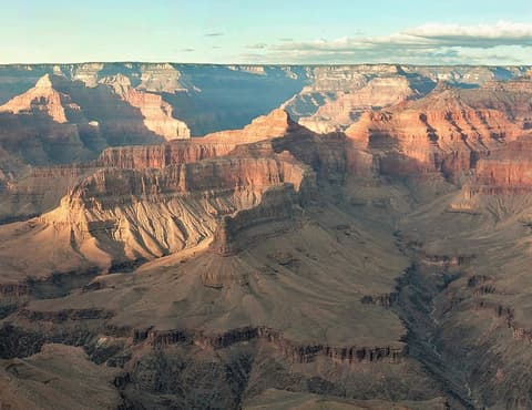 A sweeping aerial panoramic view of Grand Canyon's layered red rock formations and deep shadowed canyon depths.