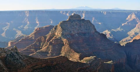 Vishnu Temple rises dramatically from the Grand Canyon's inner canyon, with distant snow-capped mountains on the horizon.