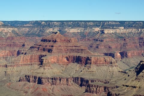 Sweeping panoramic view of Grand Canyon's layered red rock buttes and mesas with the North Rim visible in the distance.
